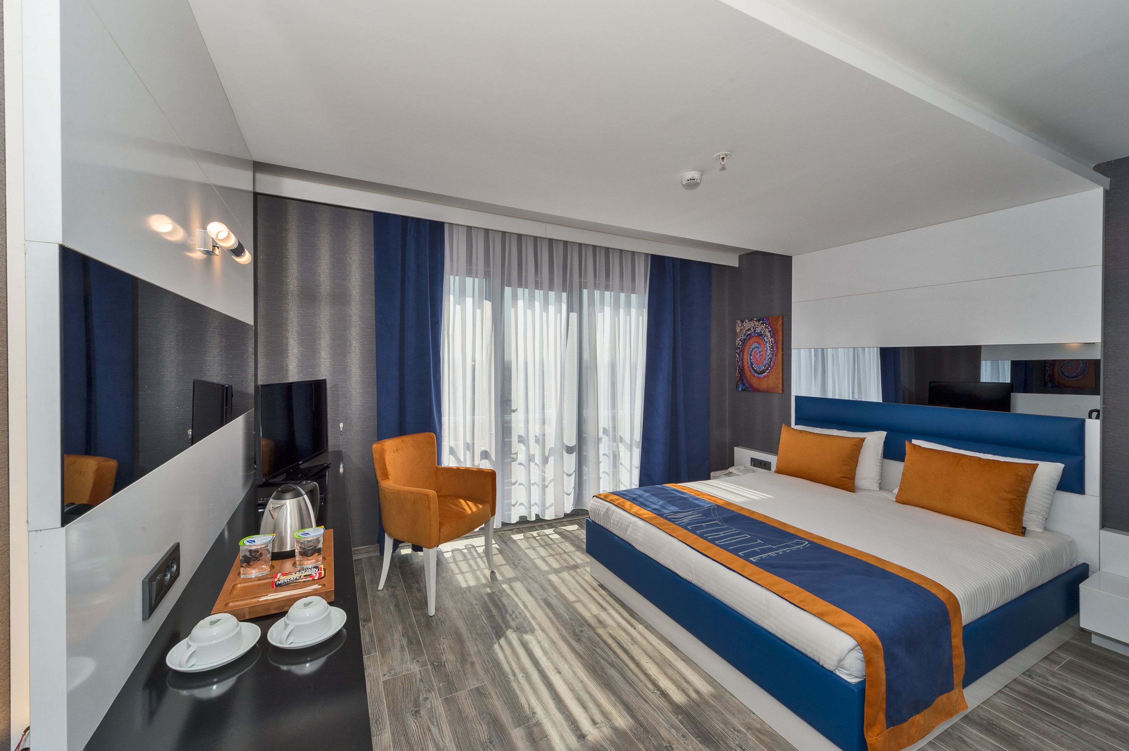 A modern hotel room with a large bed, a desk with a coffee maker, and a TV.