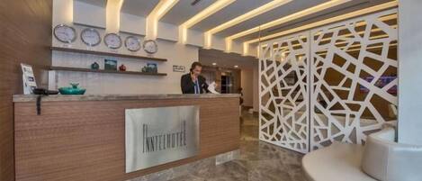 Zona de recepción de un hotel con un mostrador de madera, un reloj y una decoración en la pared.