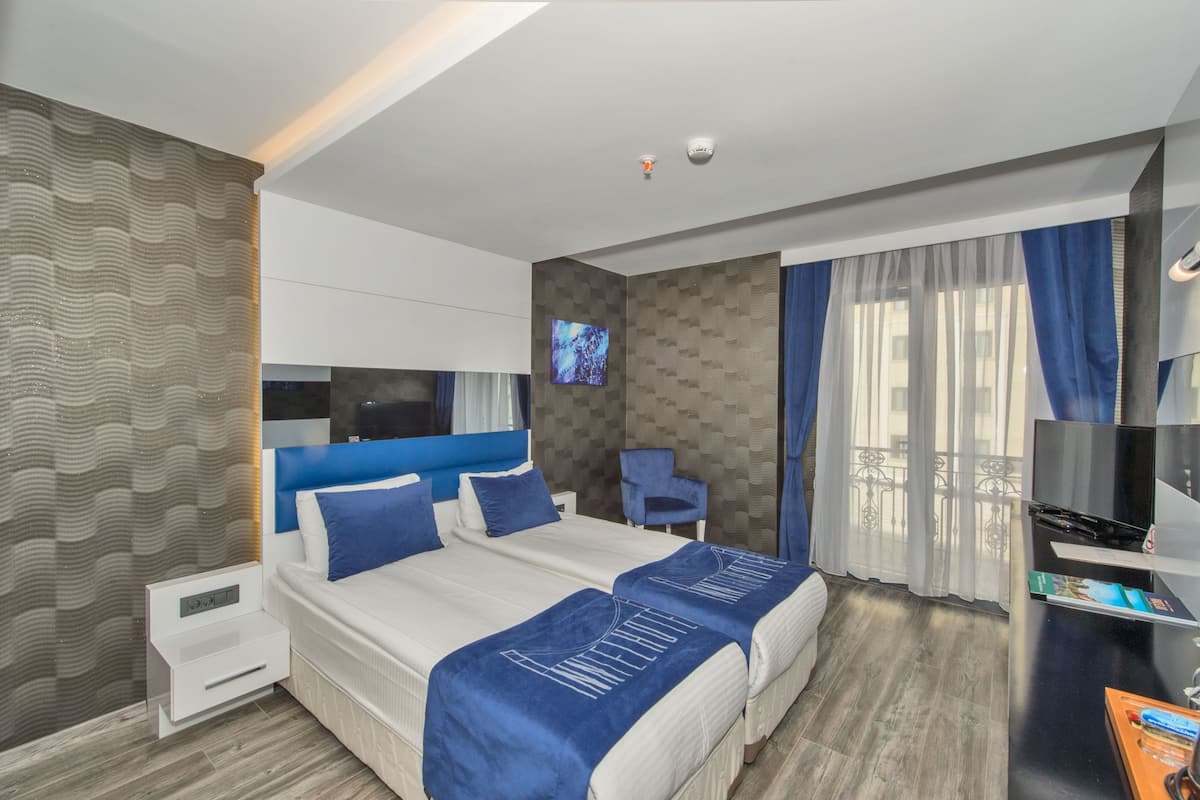 Une chambre d’hôtel avec deux lits, un bureau, une télévision et un balcon avec des rideaux.