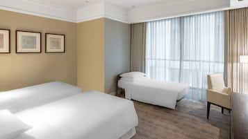 A hotel room with two beds, a desk, a chair, and a large window with curtains.