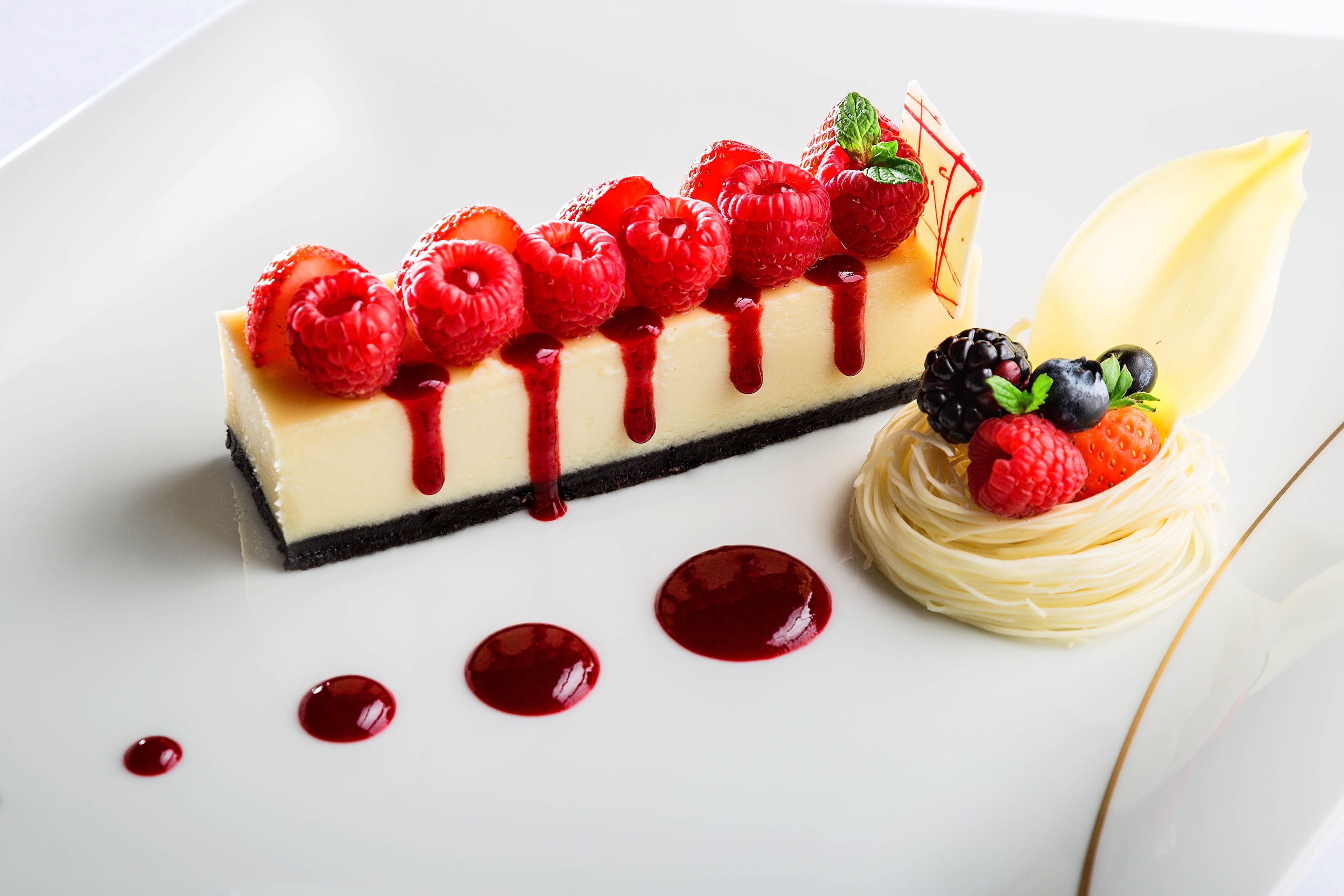 A dessert with a creamy base, topped with strawberries, raspberries, and blackberries, and drizzled with red sauce.