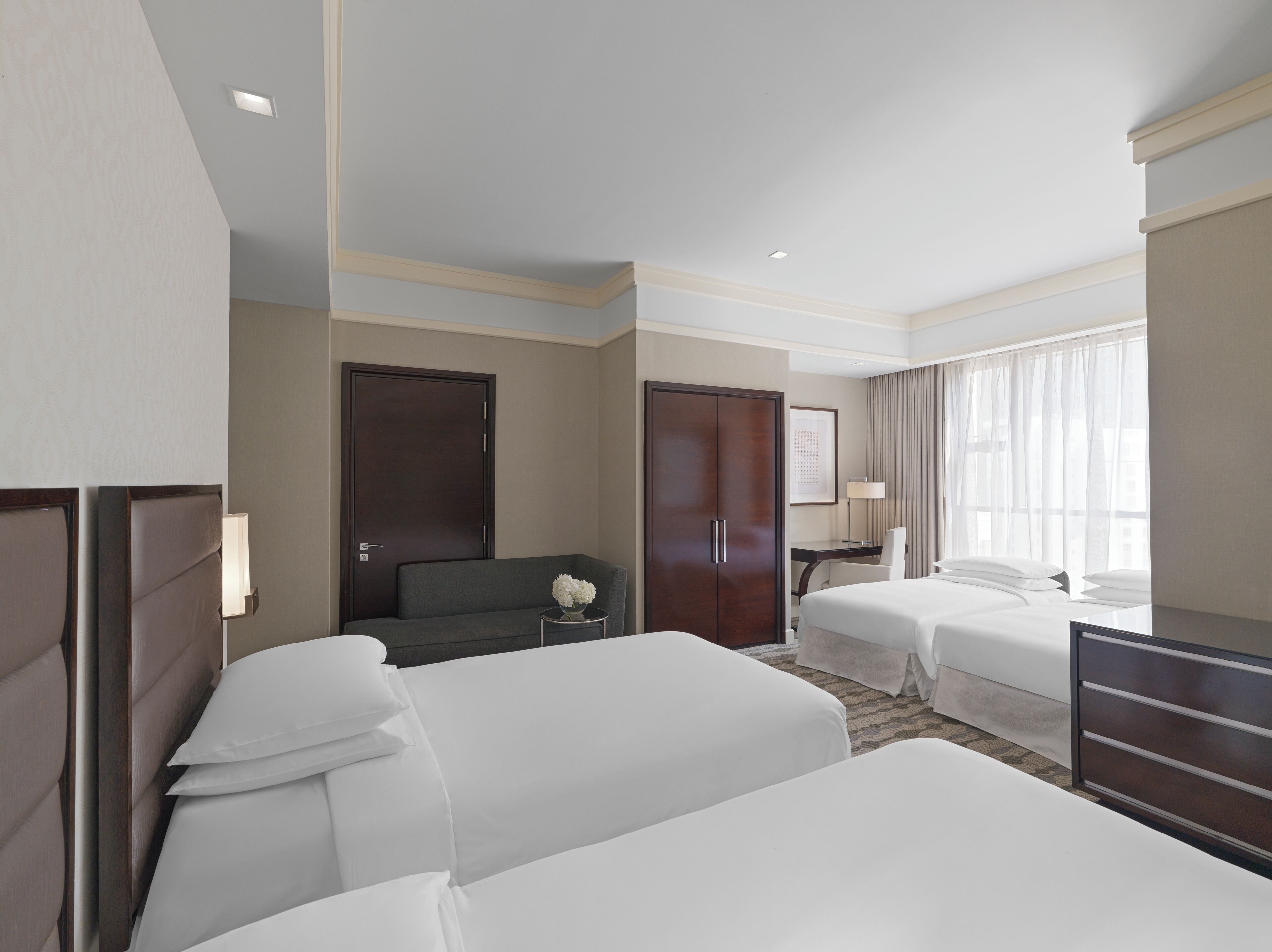 Habitació d'hotel amb dos llits, una taula, una cadira, un armari i una finestra amb cortines.