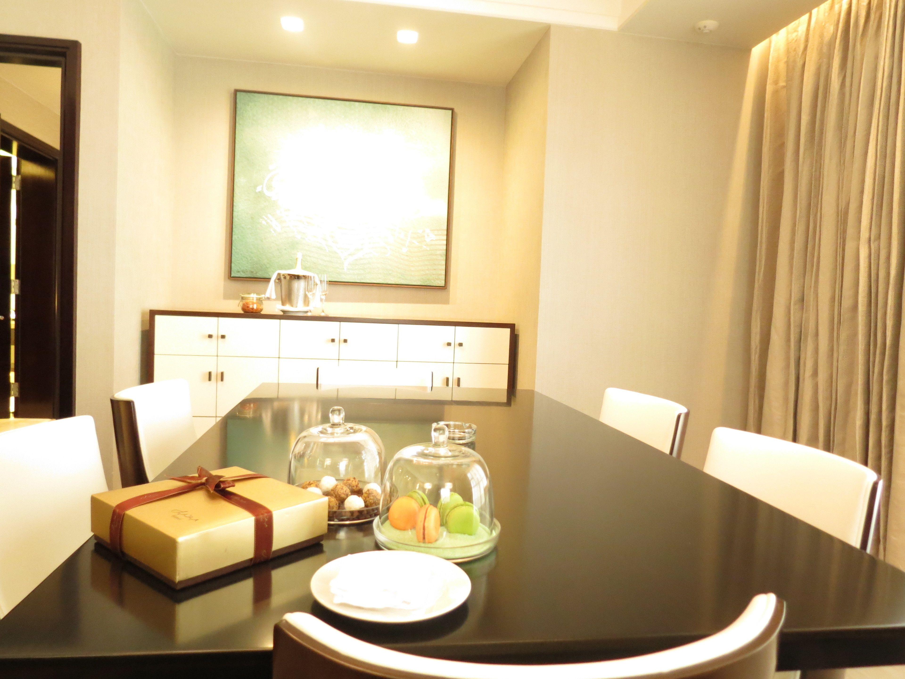 A dining table with a gift box, a glass dome with macarons, and a plate.