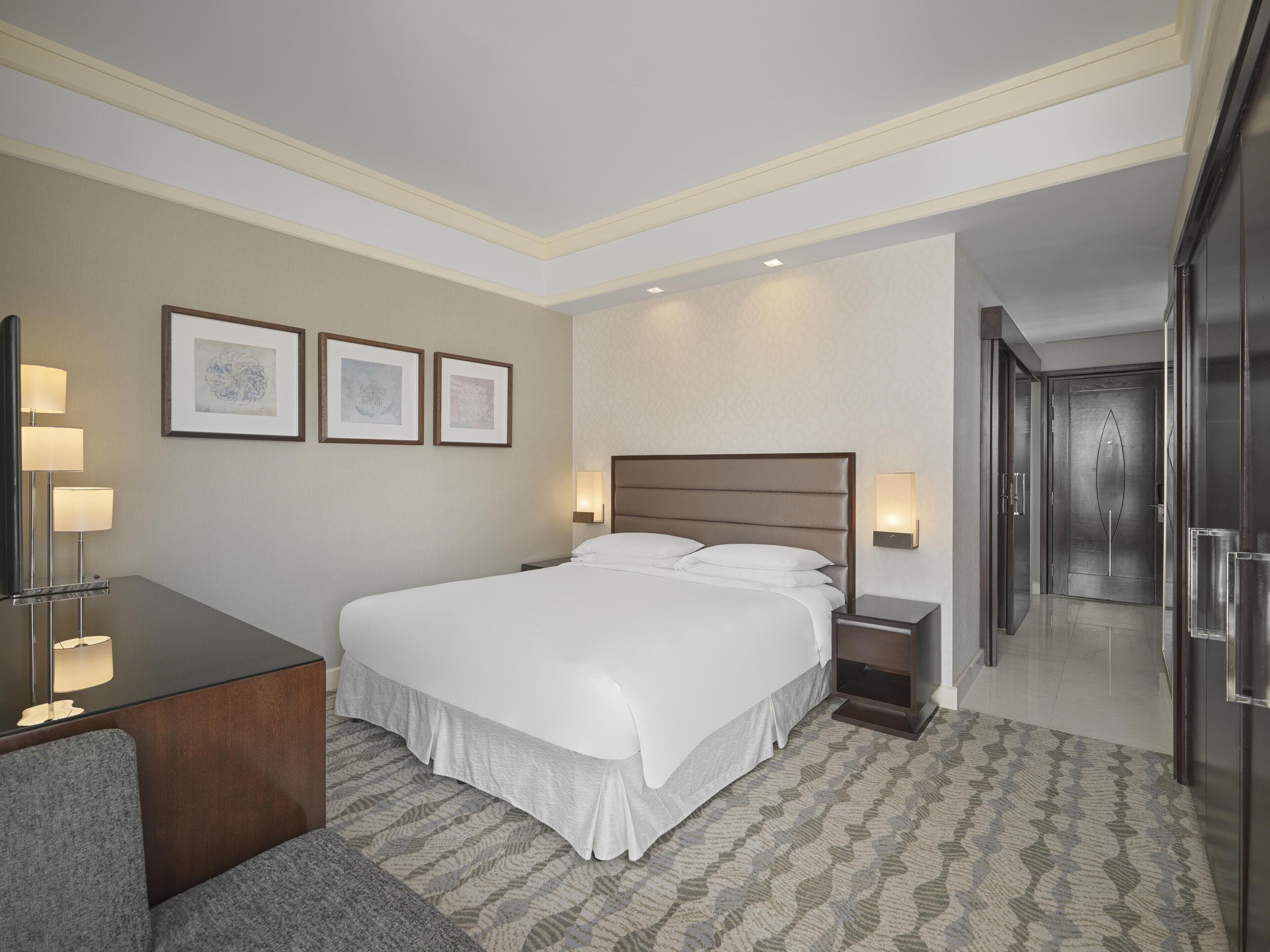 Una habitación de hotel con una cama grande, lámparas de noche, un escritorio y cuadros en la pared.