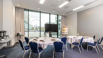 A conference room with a large table, chairs, a projector, and a view of a Ferris wheel through large windows.
