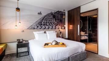 A modern hotel room with a large bed, bedside table, and a wall-mounted artwork.