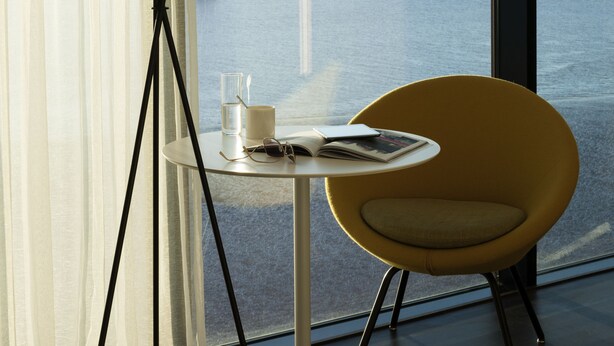 Una habitación con un ventanal grande, una lámpara de pie, un sillón amarillo redondo y una mesita con un vaso de agua y un libro.
