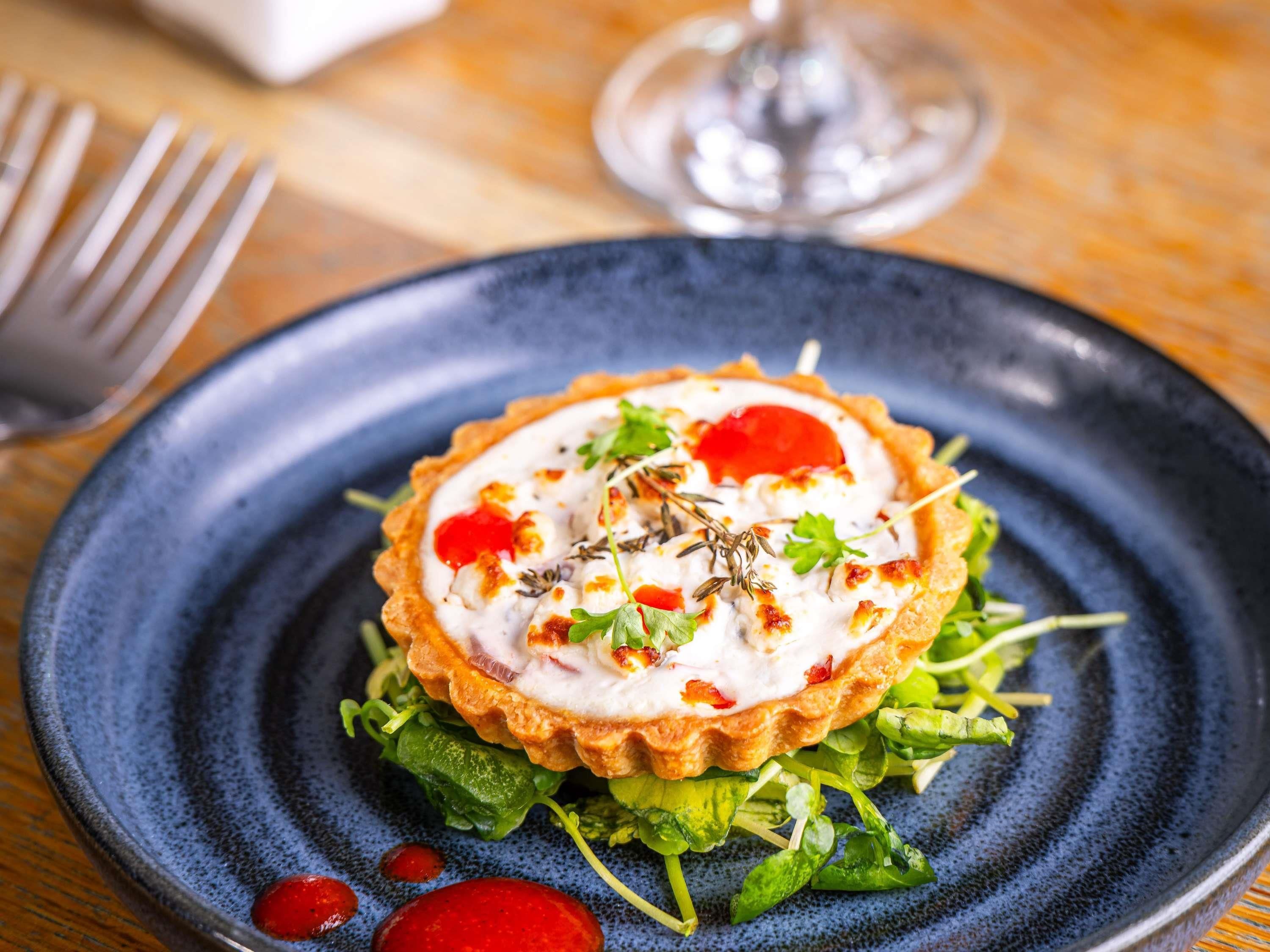 A plate with a tart, greens, and a red sauce.