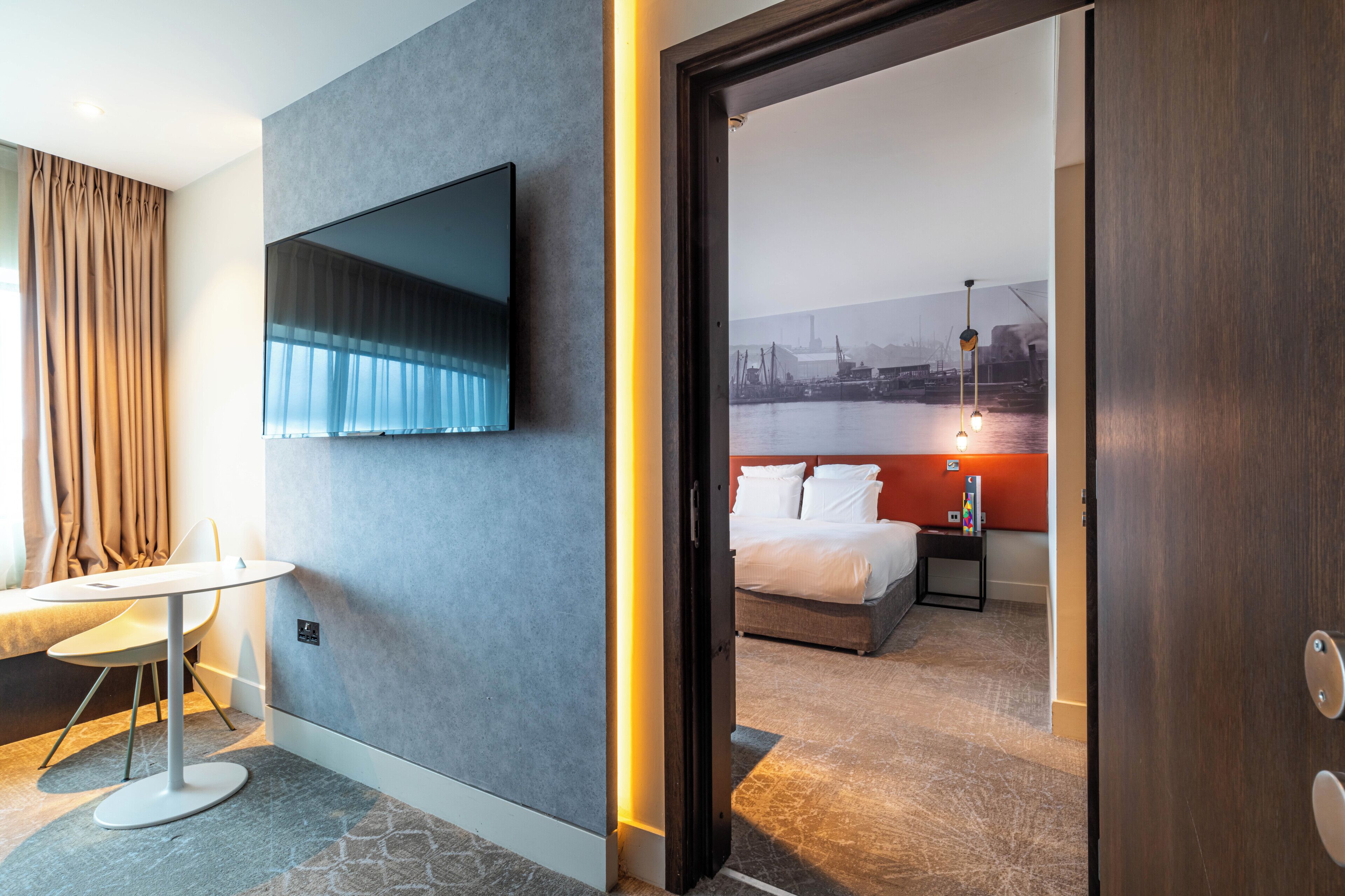Une chambre d’hôtel avec un lit, un téléviseur fixé au mur, un bureau et une vue sur un port.
