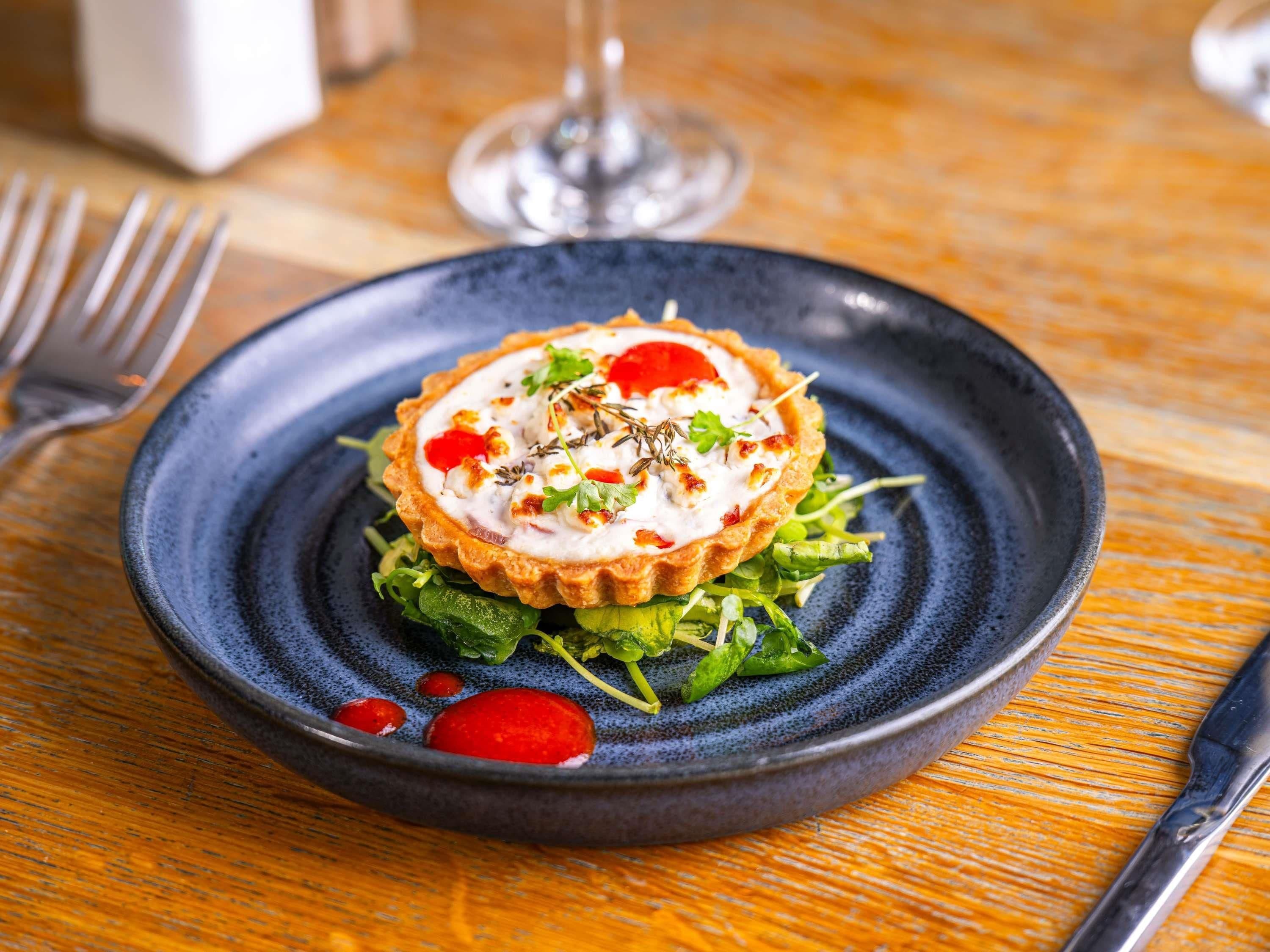 A plate with a tart and greens on a dark blue plate.