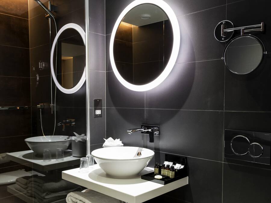 Ein modernes Badezimmer mit einem großzügigen weißen Waschbecken, einem Spiegel mit runder Beleuchtung und einer Duschkabine.