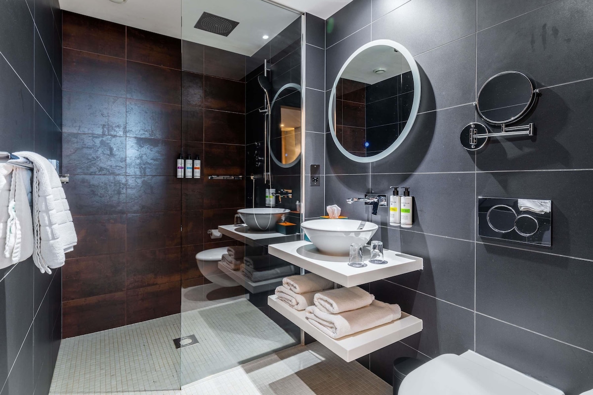 A modern bathroom with a glass shower enclosure, a white sink with a vessel basin, and two wall-mounted mirrors.
