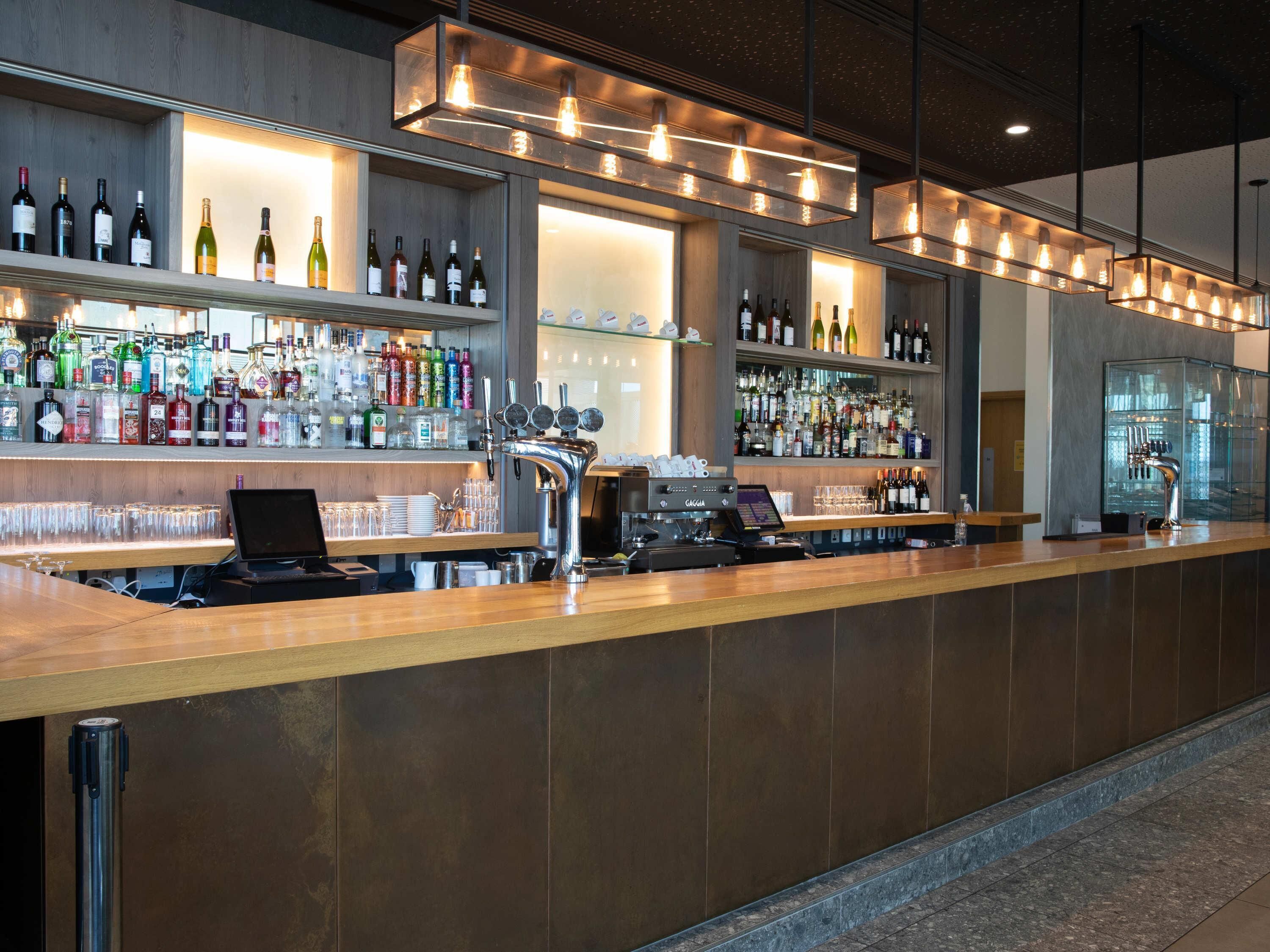 Una zona de bar con una barra larga, estantes con diferentes botellas y una máquina de café espresso Gaggia.