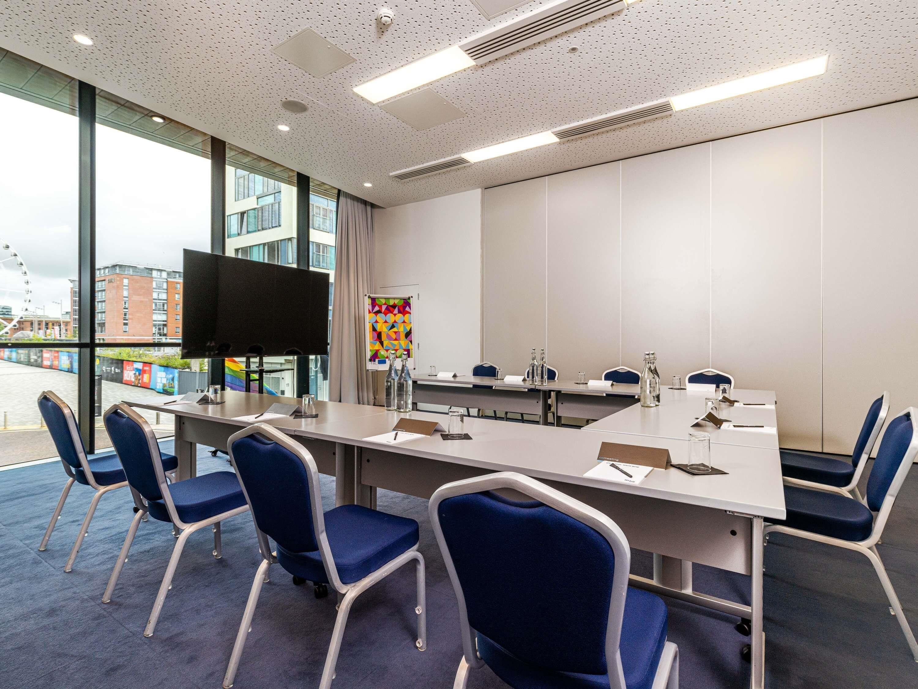 A conference room with a long table, chairs, a TV, and a poster.