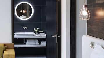 Un baño moderno con un espejo redondo, lavamanos blanco y un perchero.