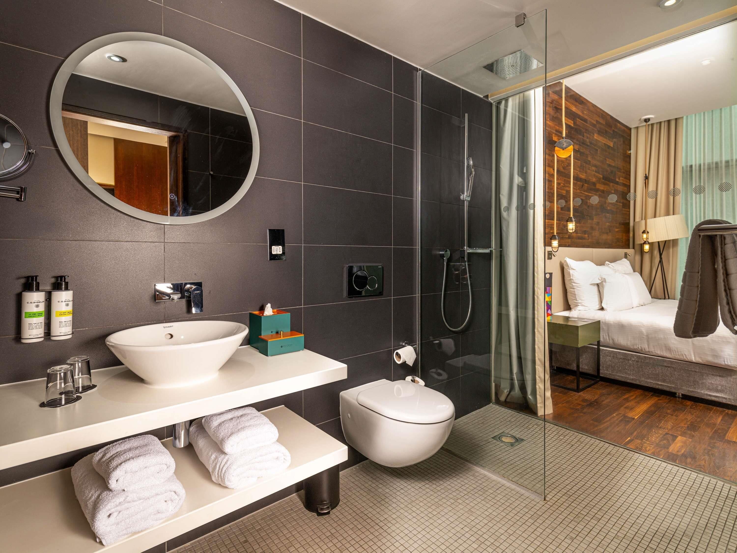 A modern bathroom with a round mirror, white sink, and a glass-enclosed shower.