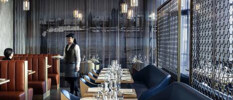 Un restaurante con asientos tipo cabina, meseros y vistas panorámicas de la ciudad.