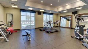 Une salle de sport équipée de tapis de course, d’haltères et d’un ballon d’exercice rouge.