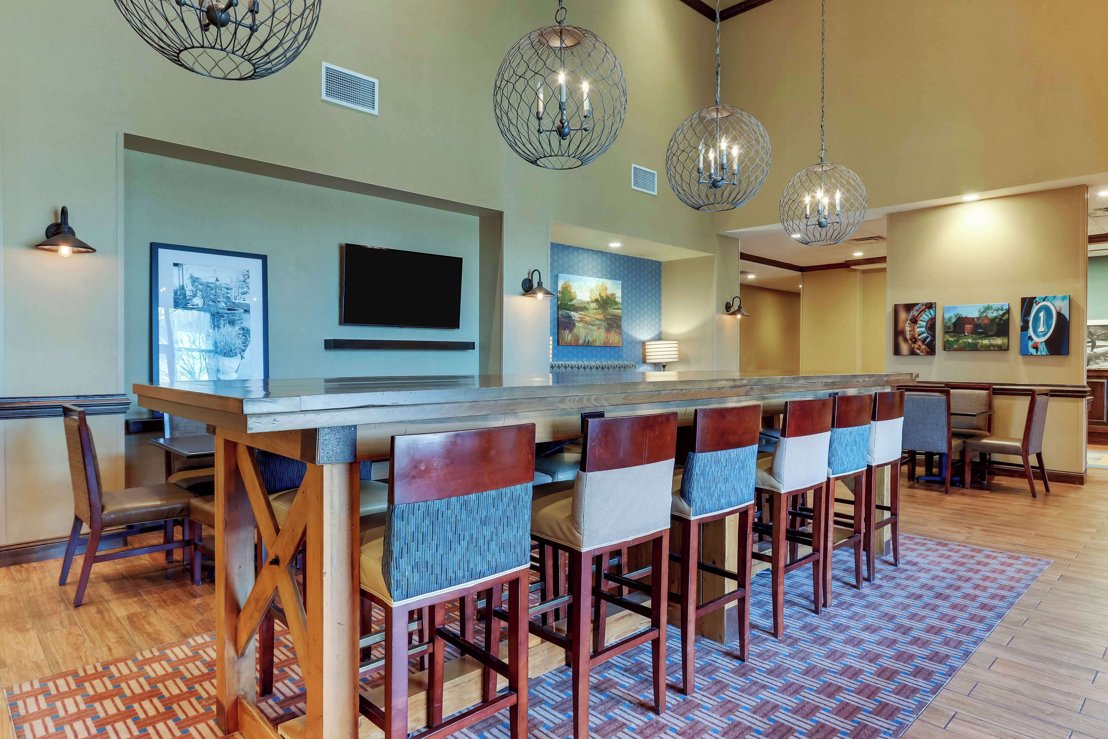 A modern dining area with a long wooden table, six chairs with cushioned seats, and decorative hanging lights.