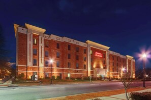 A multi-story brick building with a prominent red sign, likely a hotel, featuring a modern design with large windows and a flat roof.