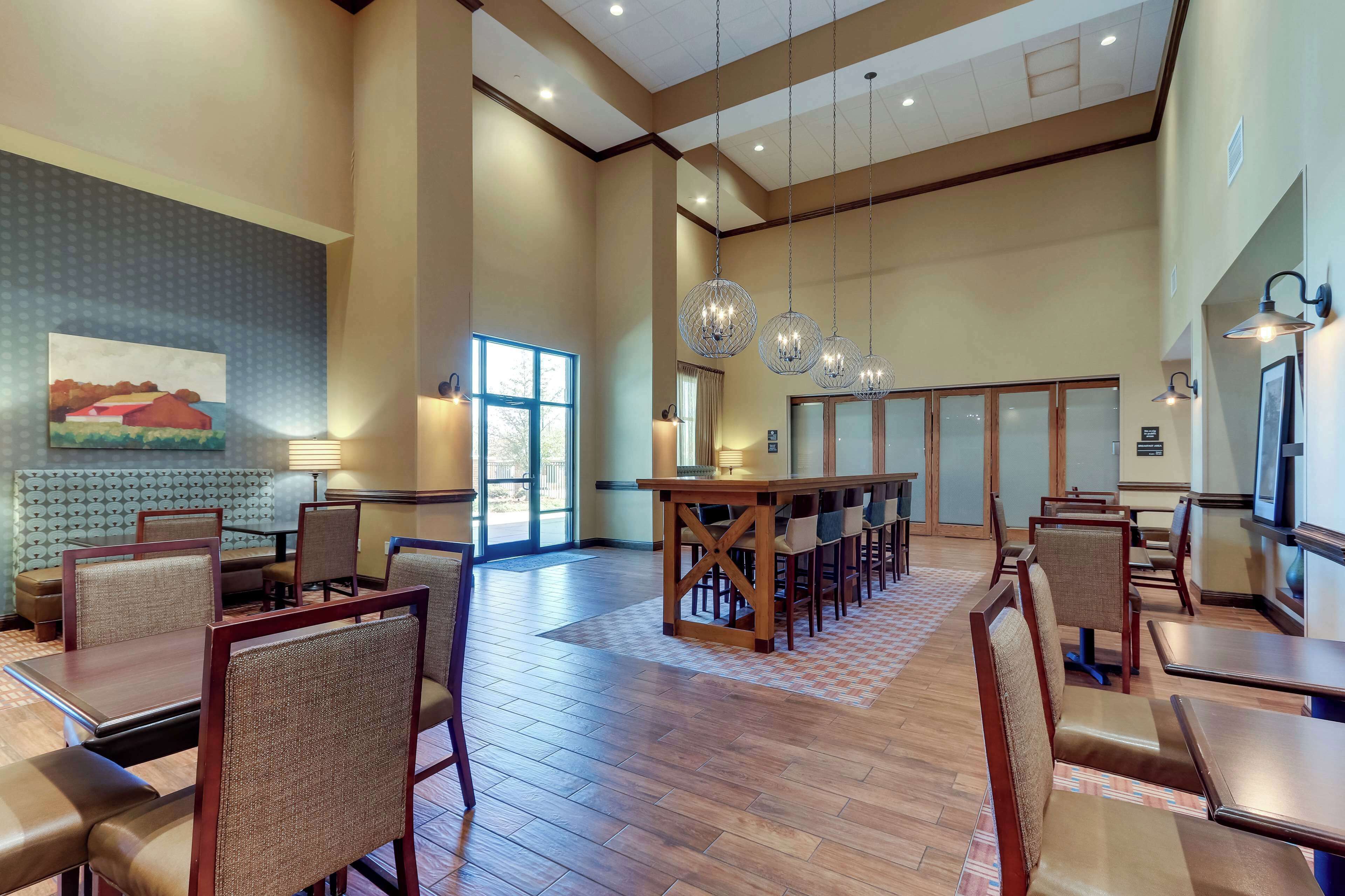 A spacious hotel lobby with a high ceiling, wooden flooring, and a central bar area.