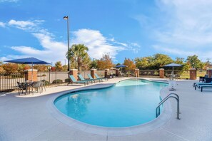 A swimming pool with lounge chairs and umbrellas, surrounded by a brick wall and trees.