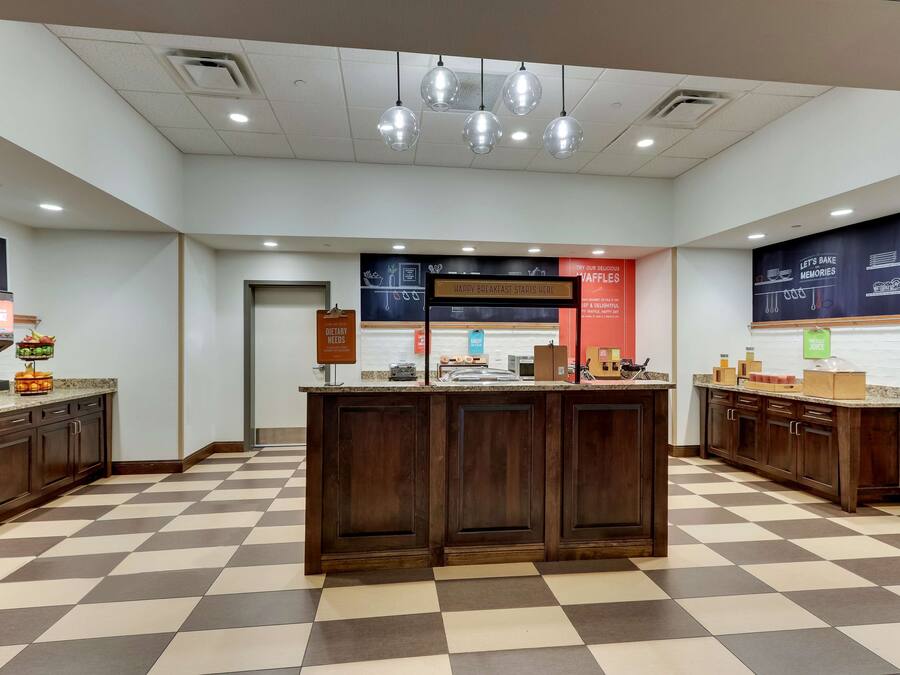 A bakery counter with a checkered floor, a sign that says "Happy Breakfast Starts Here," and a sign indicating the location of the bakery.