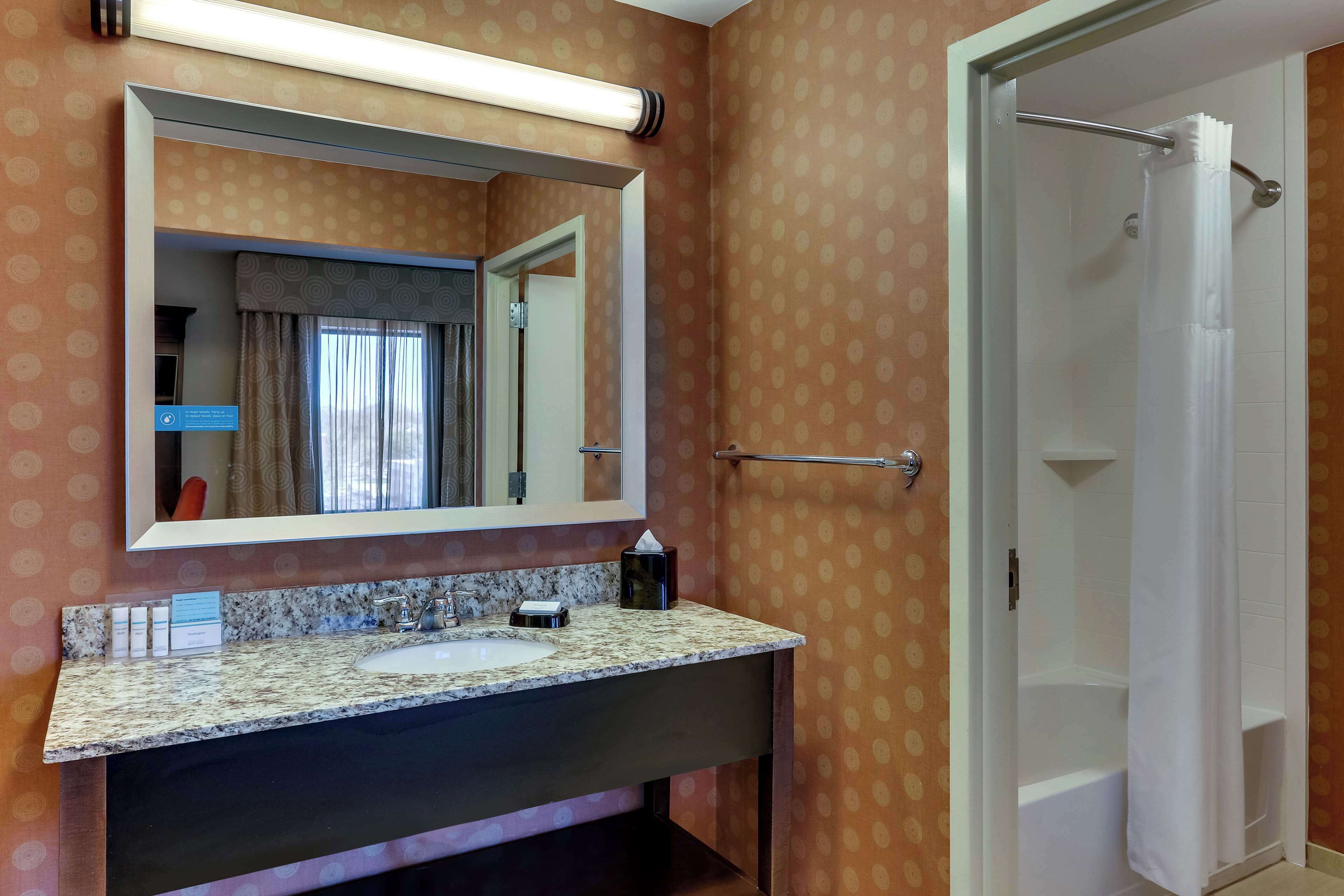 A bathroom with a granite countertop sink, a large mirror, and a shower area.