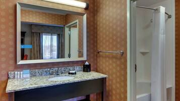 A bathroom with a granite countertop sink, a large mirror, and a shower area.