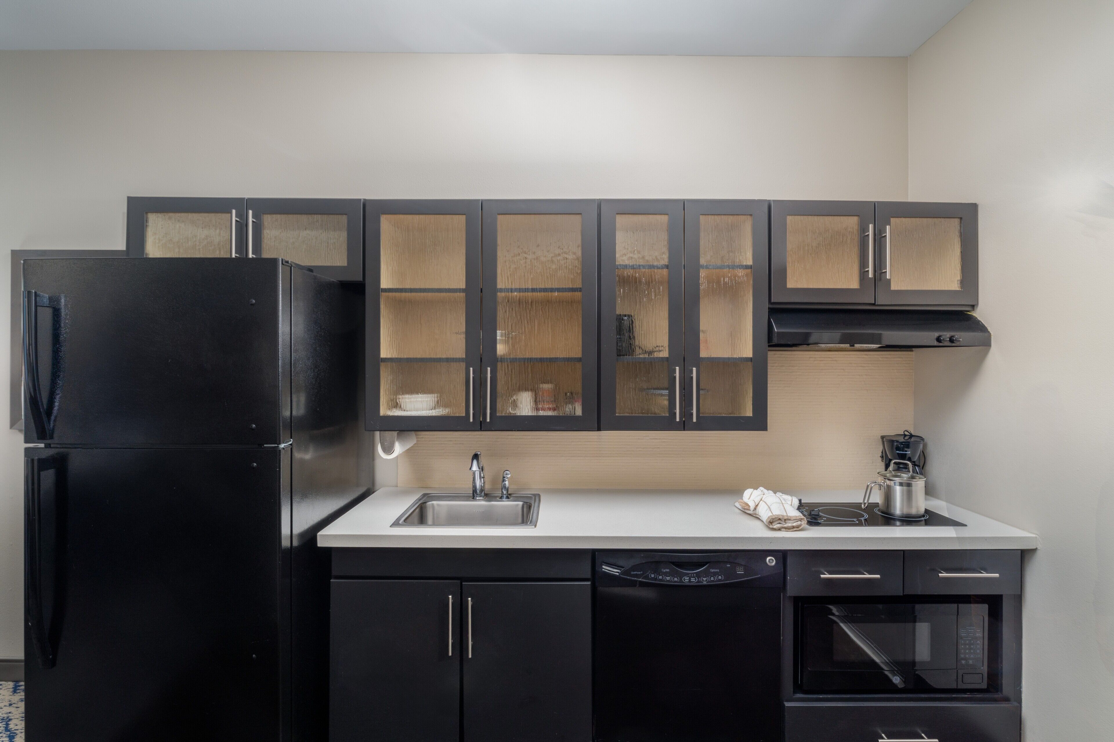 Cocina compacta con refrigerador negro, un lavamanos, cafetera y microondas.