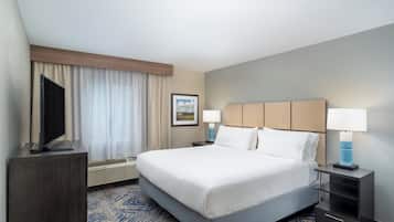 Habitación de hotel con una cama grande, dos mesitas de noche con lámparas, un televisor de pantalla plana, un cuadro en la pared y una ventana con cortinas.