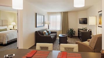 A hotel room with a bed, a sofa, a dining table, and a TV.