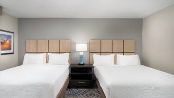 A hotel room with two single beds, a nightstand with a lamp, and a framed picture on the wall.