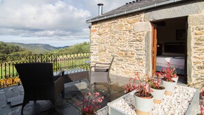 A stone building with a balcony, wicker chairs, potted plants, and a view of hills. - Casa Piñeiro (Monfero)