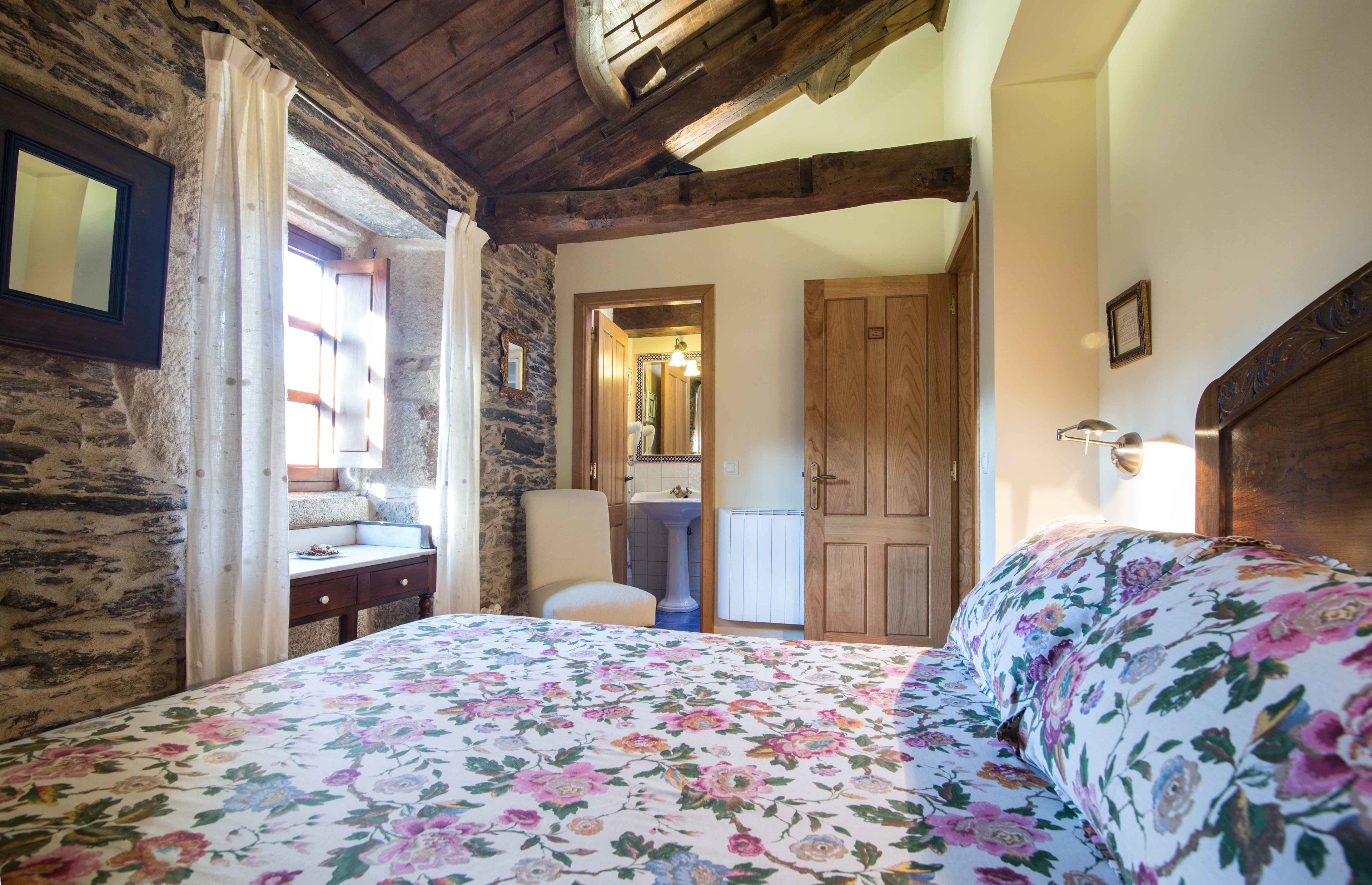 Un dormitorio con techo de madera, una cama con ropa de cama floral, un armario de madera, una mesita de noche y un espejo en la pared.