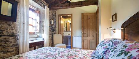 Un dormitorio con techo de madera, una cama con ropa de cama floral, un armario de madera, una mesita de noche y un espejo en la pared.