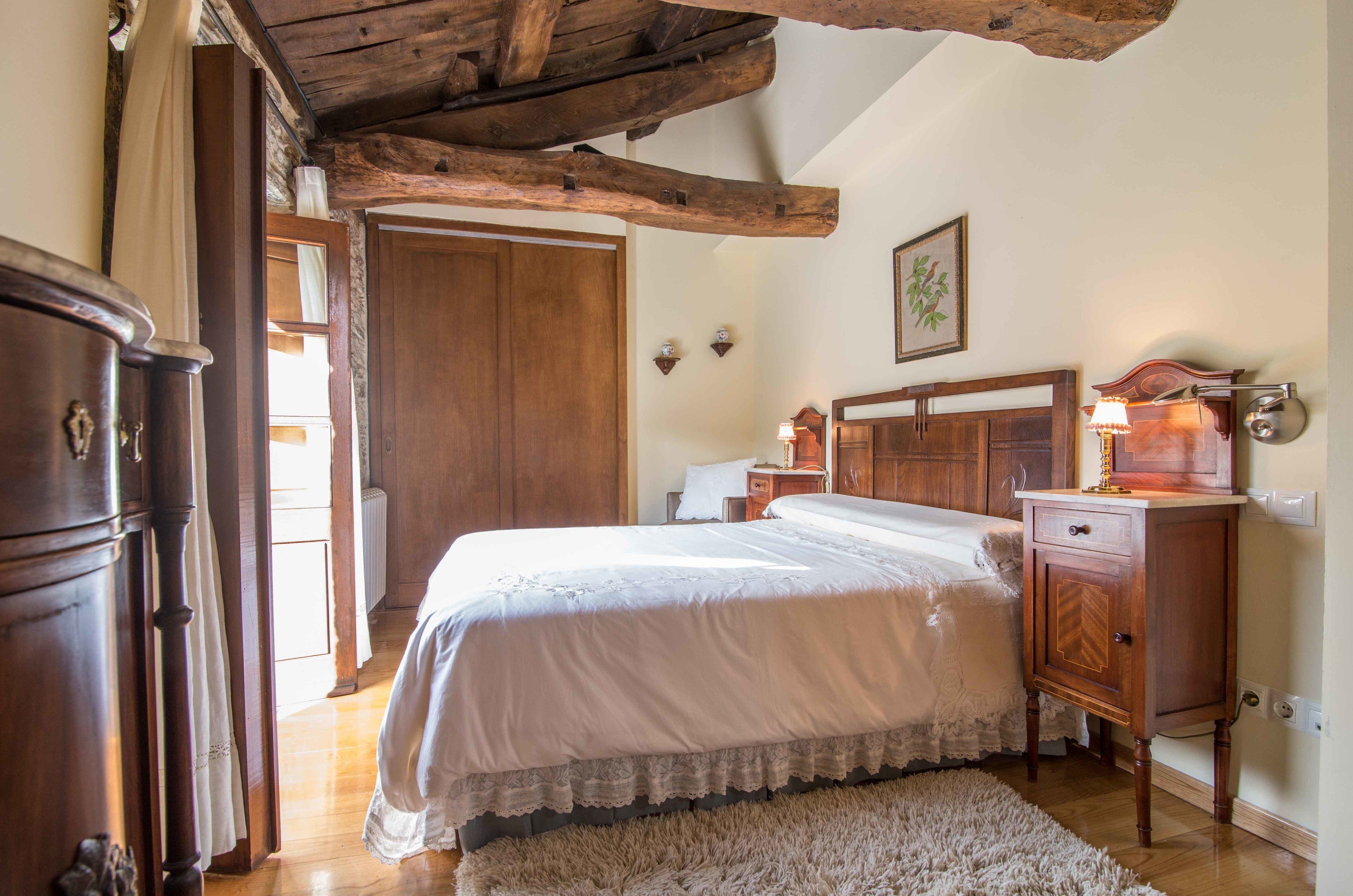 Een slaapkamer met een houten bed, nachtkastje, kast en een zichtbare houten balk in het plafond.