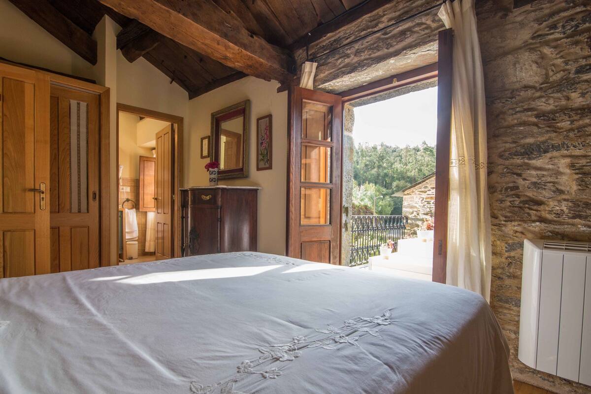 Ein Schlafzimmer mit einem großen Bett, Holzbalkendecke, einer Steinwand und Blick auf Grünland.
