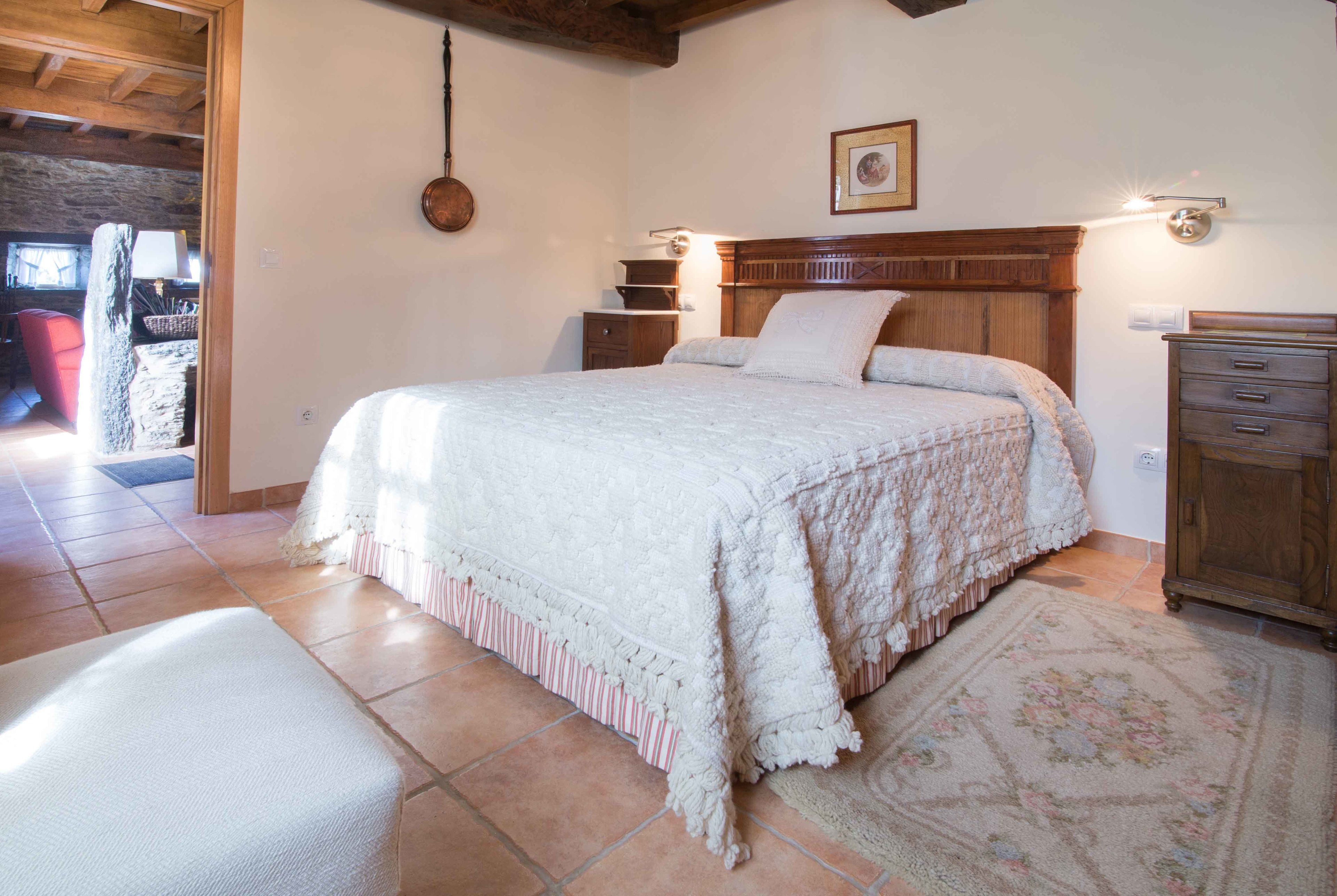 Un dormitorio con una cama grande, cabecera de madera, mesitas de noche y un pequeño mueble auxiliar.