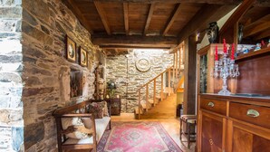 A rustic interior with stone walls, wooden beams, a staircase, and a wooden cabinet with glassware. - Casa Piñeiro (Monfero)