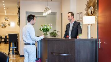 A hotel reception area with a dark wood reception desk, a large mirror, and a modern chandelier.