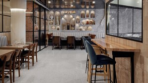 A modern dining area with wooden tables and chairs, a central island, and a decorative wall with various items. - Hôtel MOCO Valleyfield (Salaberry De Valleyfield)