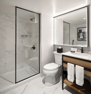 A modern bathroom with a glass-enclosed shower, a white toilet, a vanity with a mirror, and a towel rack. - Hôtel MOCO Valleyfield (Salaberry De Valleyfield)