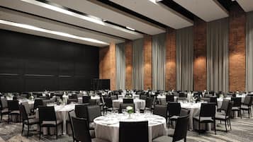 Un amplio salón de conferencias con varias mesas redondas y sillas, un techo alto con vigas a la vista y paredes de ladrillo.