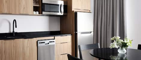 A modern kitchen with wooden cabinets, a stainless steel microwave, a dishwasher, and a dining area with a black table and chairs.
