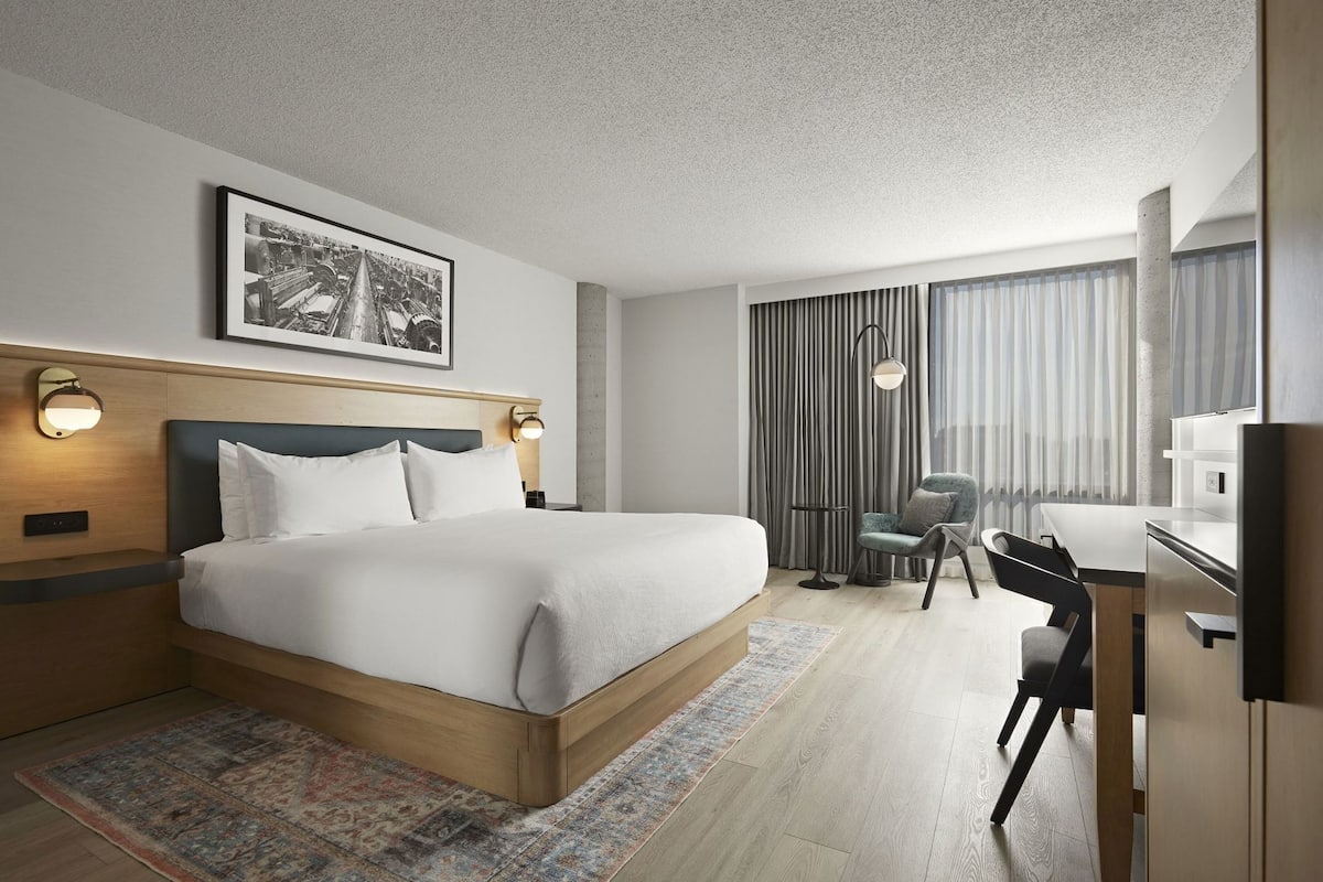 A hotel room with a large bed, a desk, a chair, a television, and a framed picture on the wall.