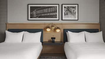 A hotel room with two beds, a wooden headboard, a nightstand with a clock, and two framed pictures on the wall.