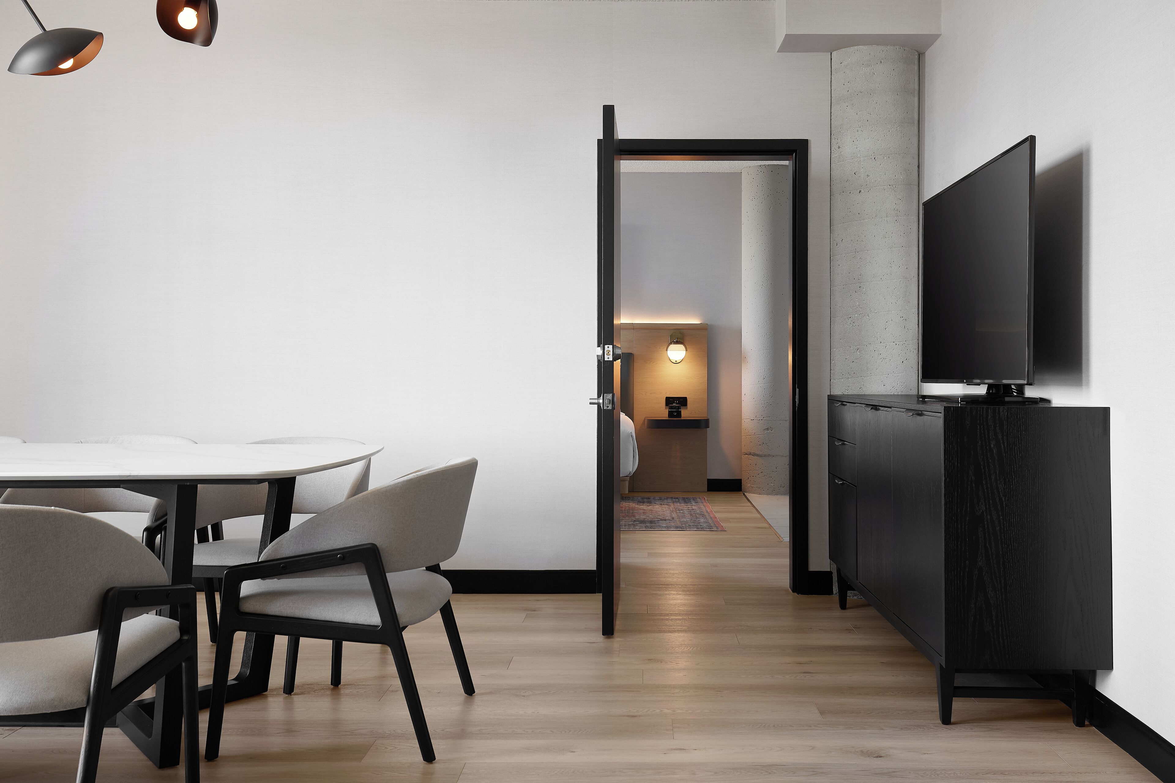 Un interior moderno con una mesa de comedor redonda, sillas grises, un armario negro y un televisor de pantalla plana montado en la pared.
