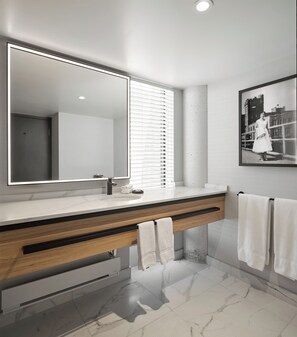 A modern bathroom with a large mirror, a wooden vanity, marble flooring, and a framed photograph on the wall. - Hôtel MOCO Valleyfield (Salaberry De Valleyfield)