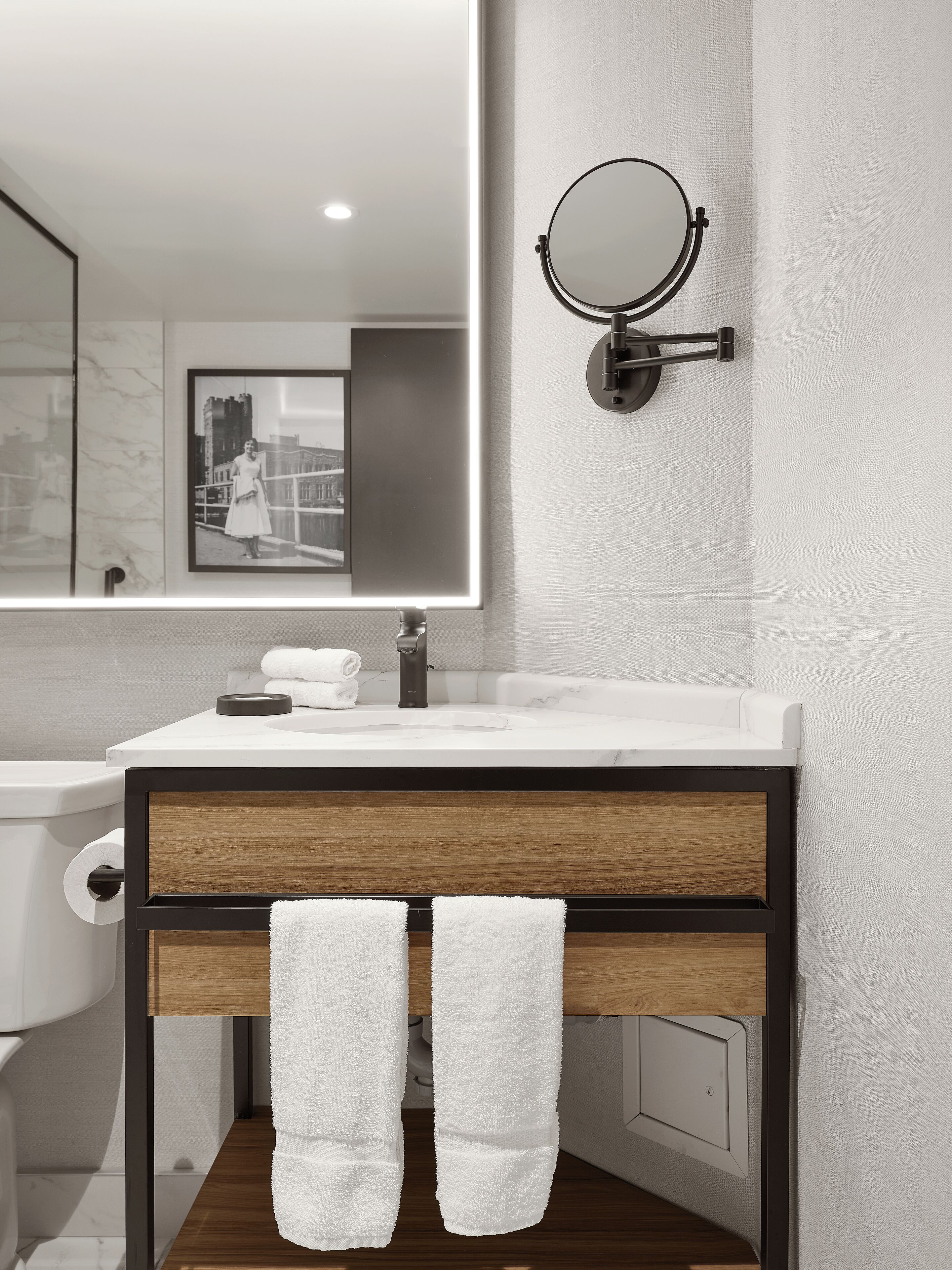 A modern bathroom with a white sink, a round mirror, and a framed picture on the wall.